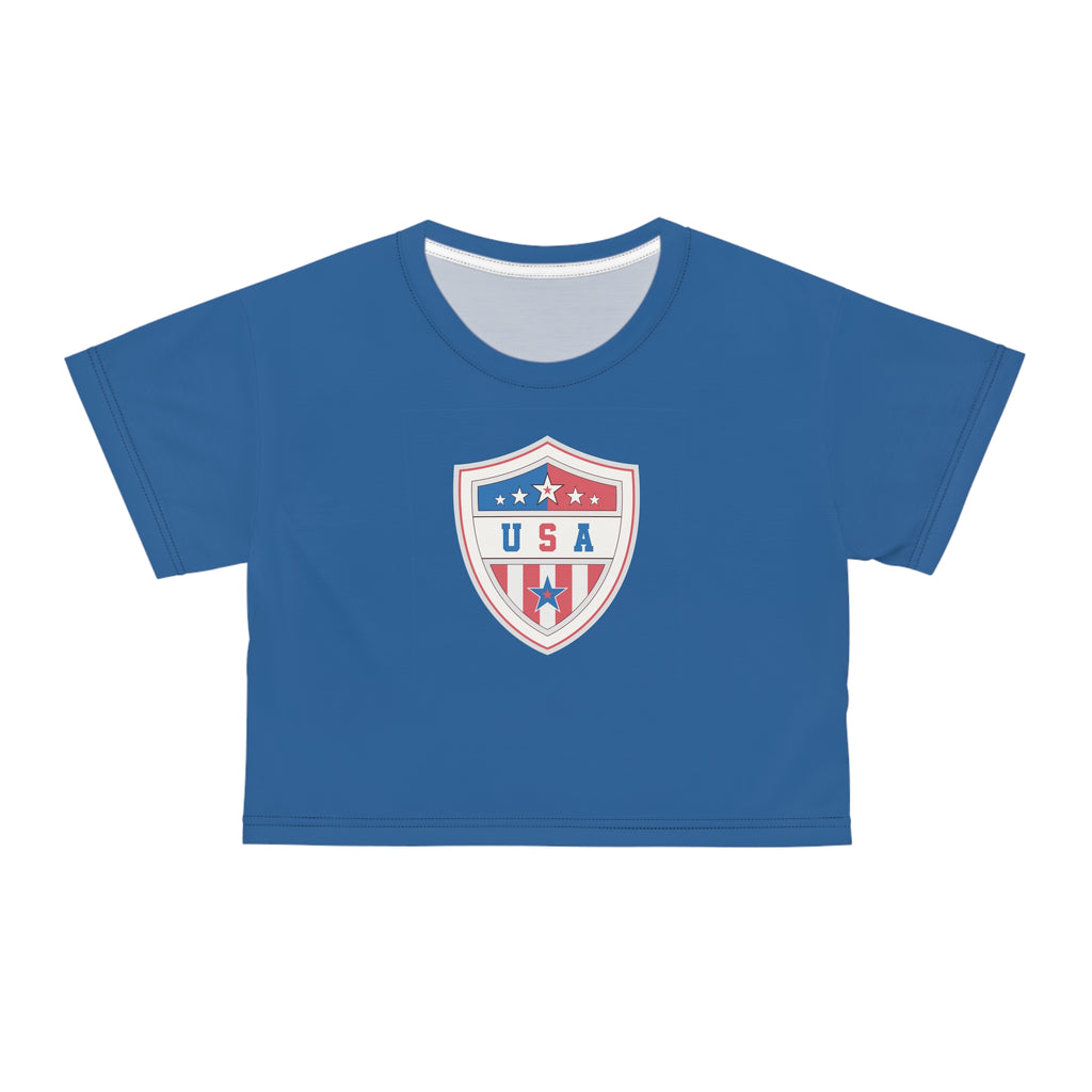 A royal blue short-sleeve crop top t-shirt featuring a USA shield crest graphic on the chest, displayed against a solid white background.