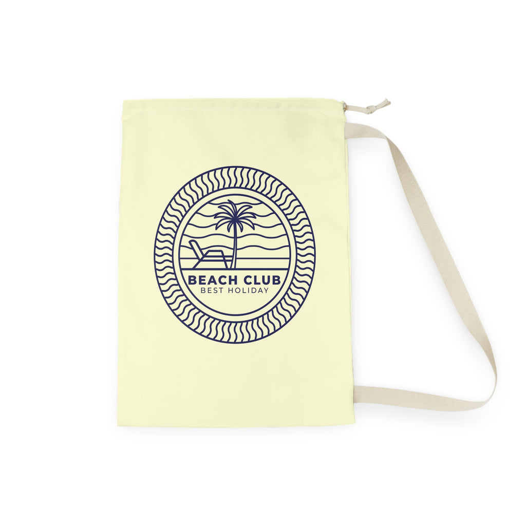 A pale yellow canvas shoulder bag with a cream strap, featuring a navy blue circular graphic on the front that reads 'BEACH CLUB BEST HOLIDAY' with a palm tree and lounge chair design.