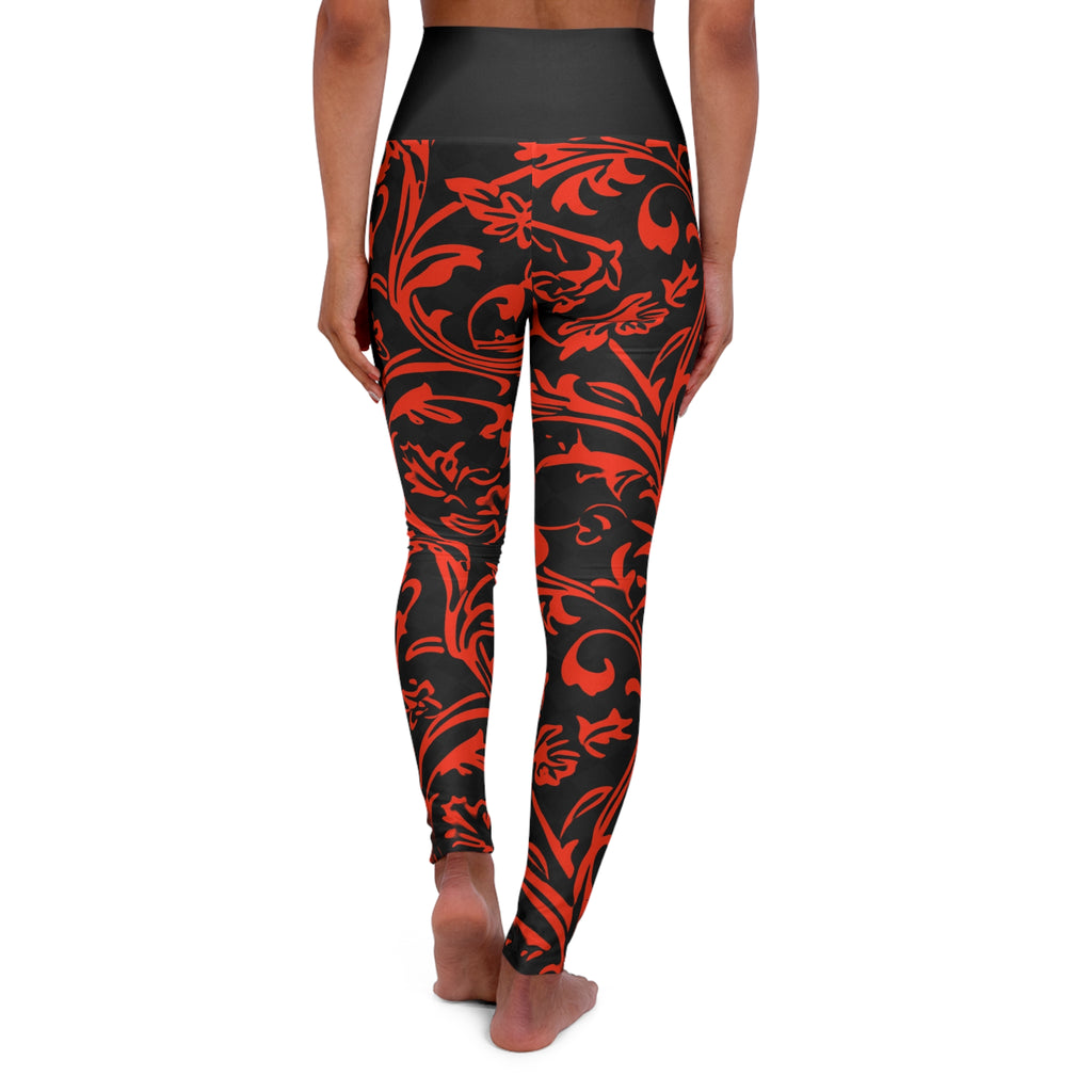 A person shown from the back wearing high-waisted leggings with a black base and a bold red ornamental floral pattern, standing barefoot against a plain white background.