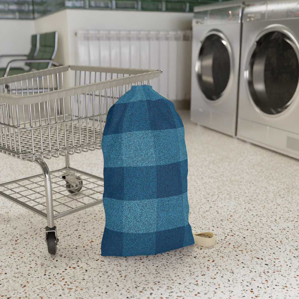 A blue and navy buffalo plaid laundry bag standing on a speckled floor next to a metal shopping cart, with washing machines in the background.
