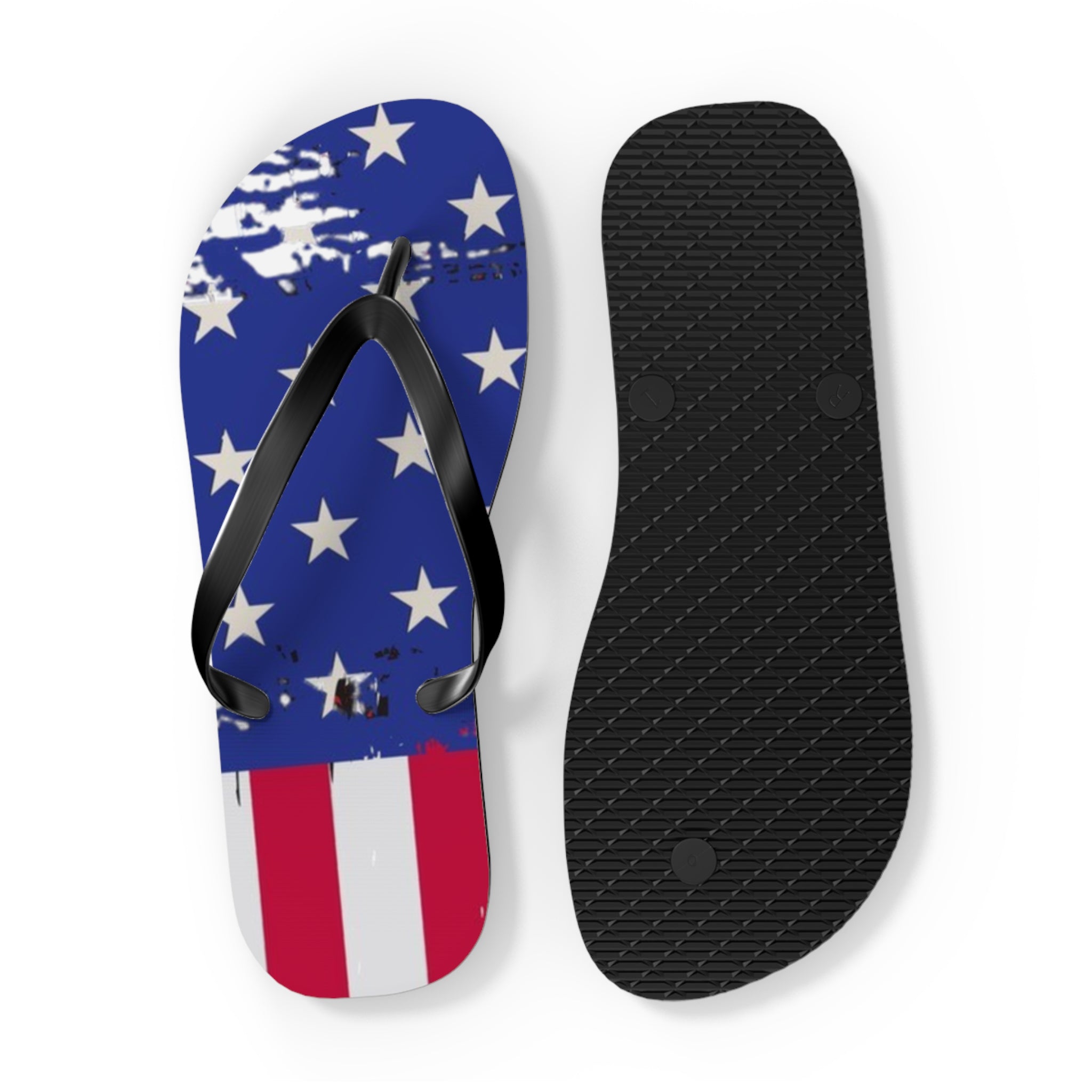 A pair of flip-flops shown on a white background, with one sandal upright displaying a distressed American flag design in blue, white, and red, and the other showing the black textured sole.
