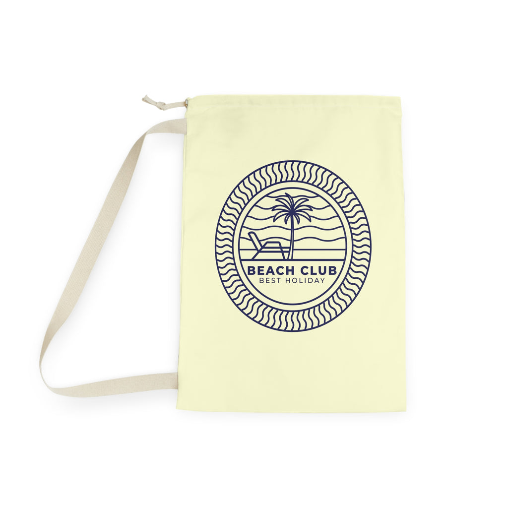 A pale yellow canvas tote bag with a beige shoulder strap, featuring a navy blue circular graphic on the front with a palm tree, beach chair, and the text 'BEACH CLUB BEST HOLIDAY'.