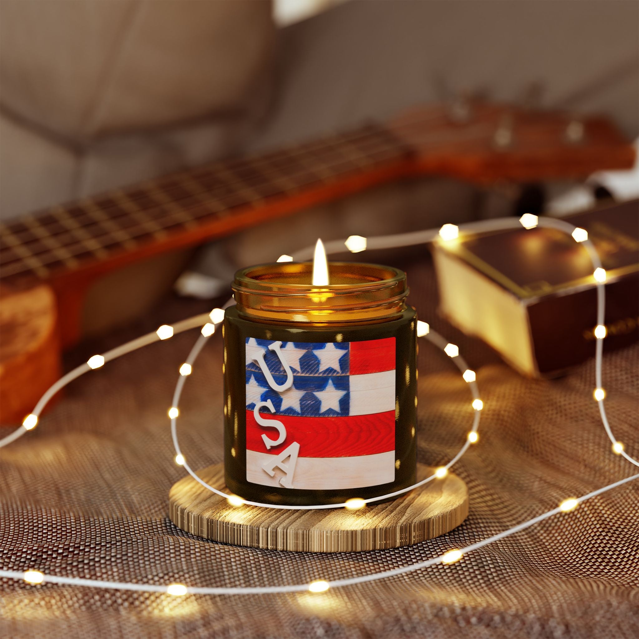 Candle with USA label on a wooden coaster surrounded by string lights, with a guitar in the background.