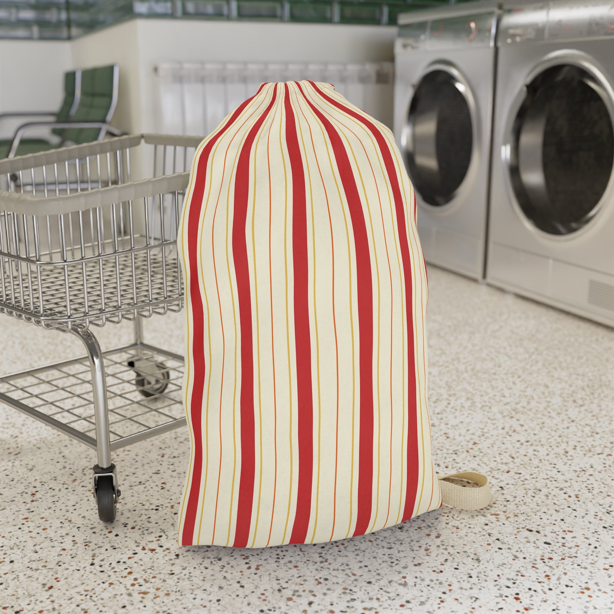 A striped laundry bag or sock holder with vertical red and cream stripes, standing on a speckled laundry room floor next to a metal shopping cart with washing machines in the background.