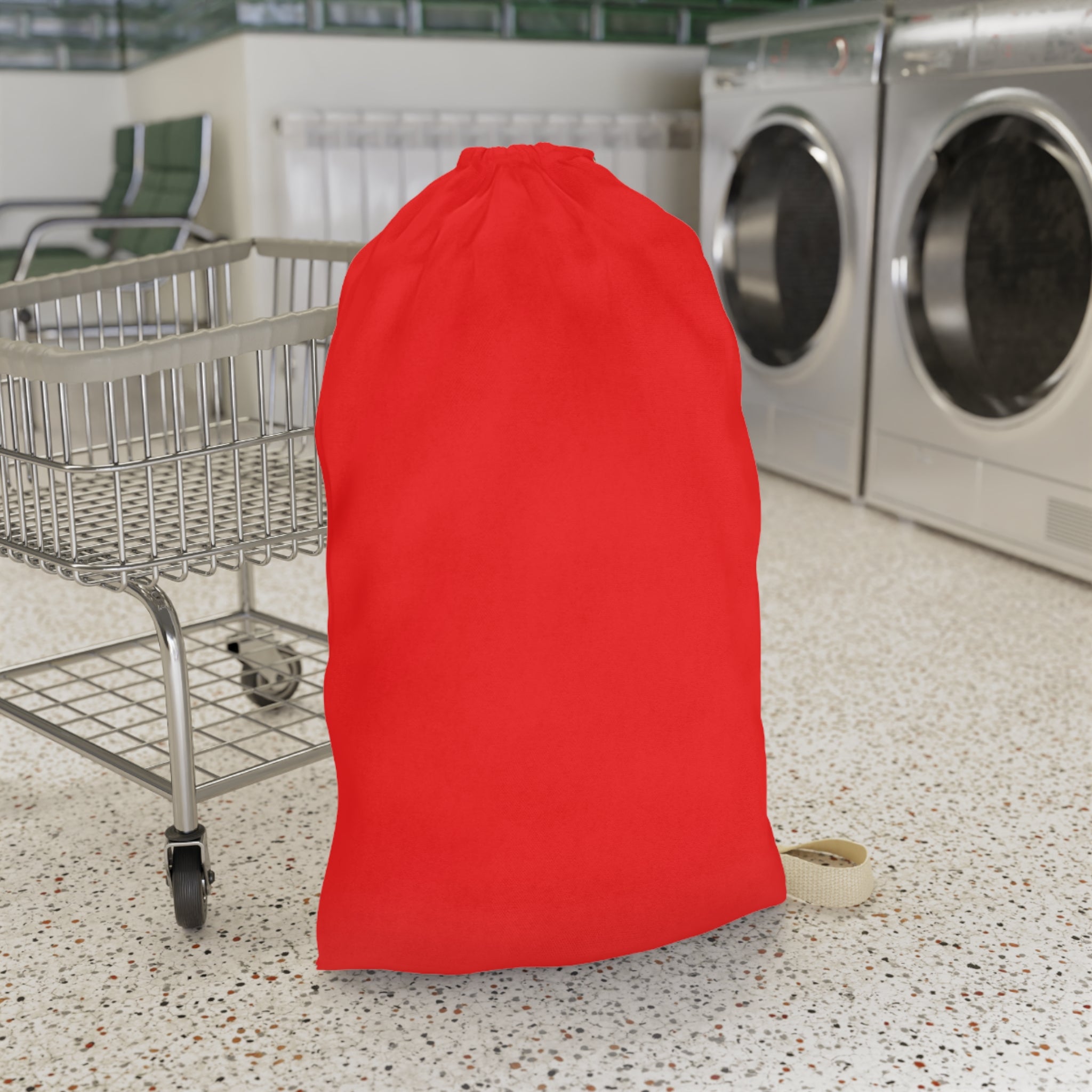 A bright red drawstring laundry bag standing upright on a speckled floor next to a metal shopping cart, with washing machines in the background.