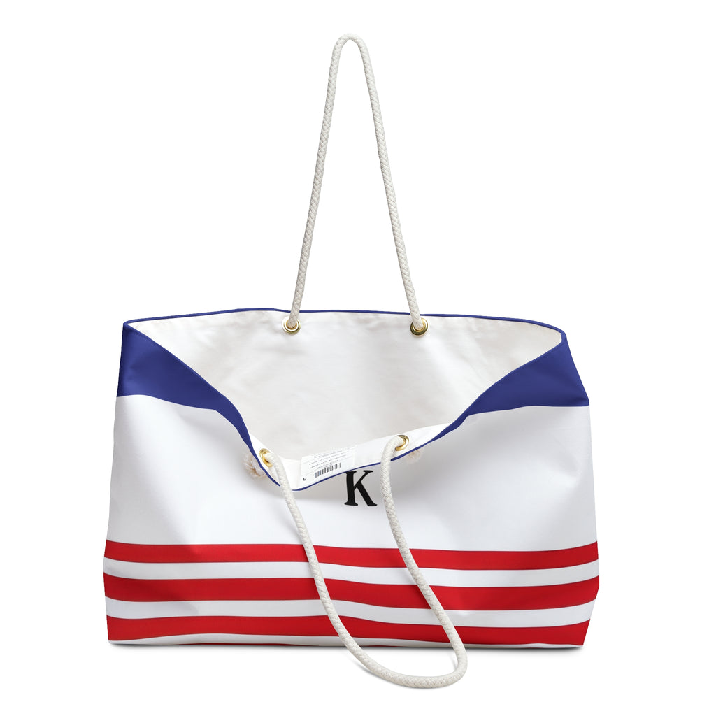 A canvas tote bag with a white, blue, and red nautical stripe design, featuring white rope handles and a black monogram 'K' on the front.