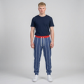 A male model standing against a light gray studio background, wearing a navy blue t-shirt, blue pinstriped sweatpants with a red drawstring waist, and white sneakers.