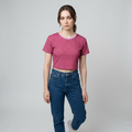 A woman modeling a short-sleeve cropped t-shirt with a textured magenta pattern and blue jeans, standing against a light gray studio background.
