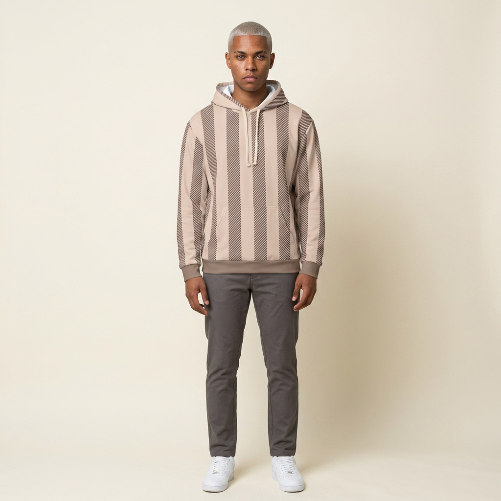 A man modeling a beige and brown vertically striped knit hoodie with a white drawstring, paired with dark gray pants and white sneakers, against a solid cream background.