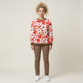 A model stands against a light beige studio background wearing a red and white floral long-sleeve sweatshirt, brown pants, and white sneakers.