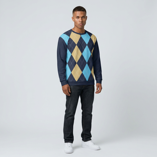 A man modeling a long-sleeve crewneck sweater with a navy blue base and an argyle pattern in light blue, tan, and navy, paired with dark jeans and white sneakers against a light gray studio background.