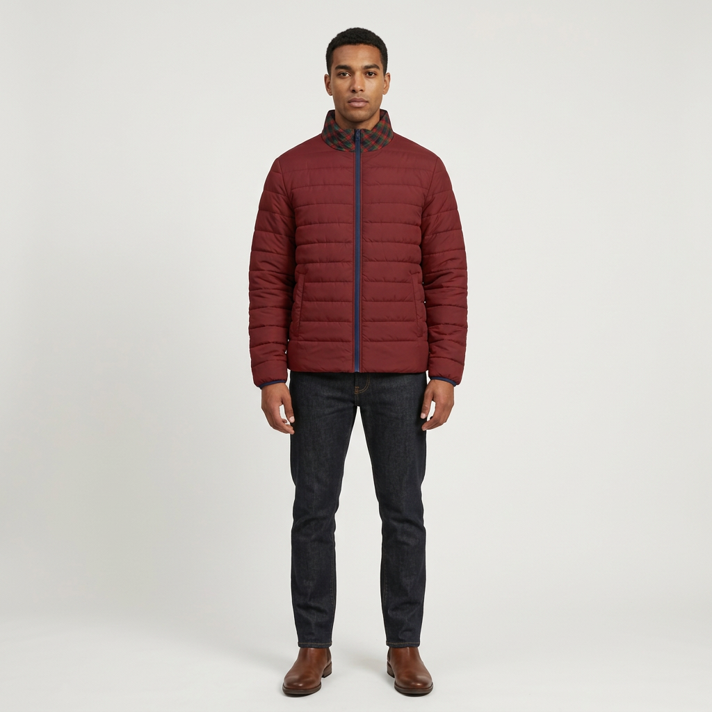 A man wearing a burgundy quilted puffer jacket with a dark patterned plaid collar, paired with dark jeans and brown leather shoes, standing against a light gray studio background.