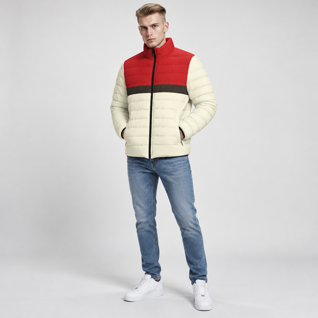 A man modeling a color-blocked puffer jacket with cream, red, and dark brown horizontal color blocks, paired with blue jeans and white sneakers against a light gray studio background.