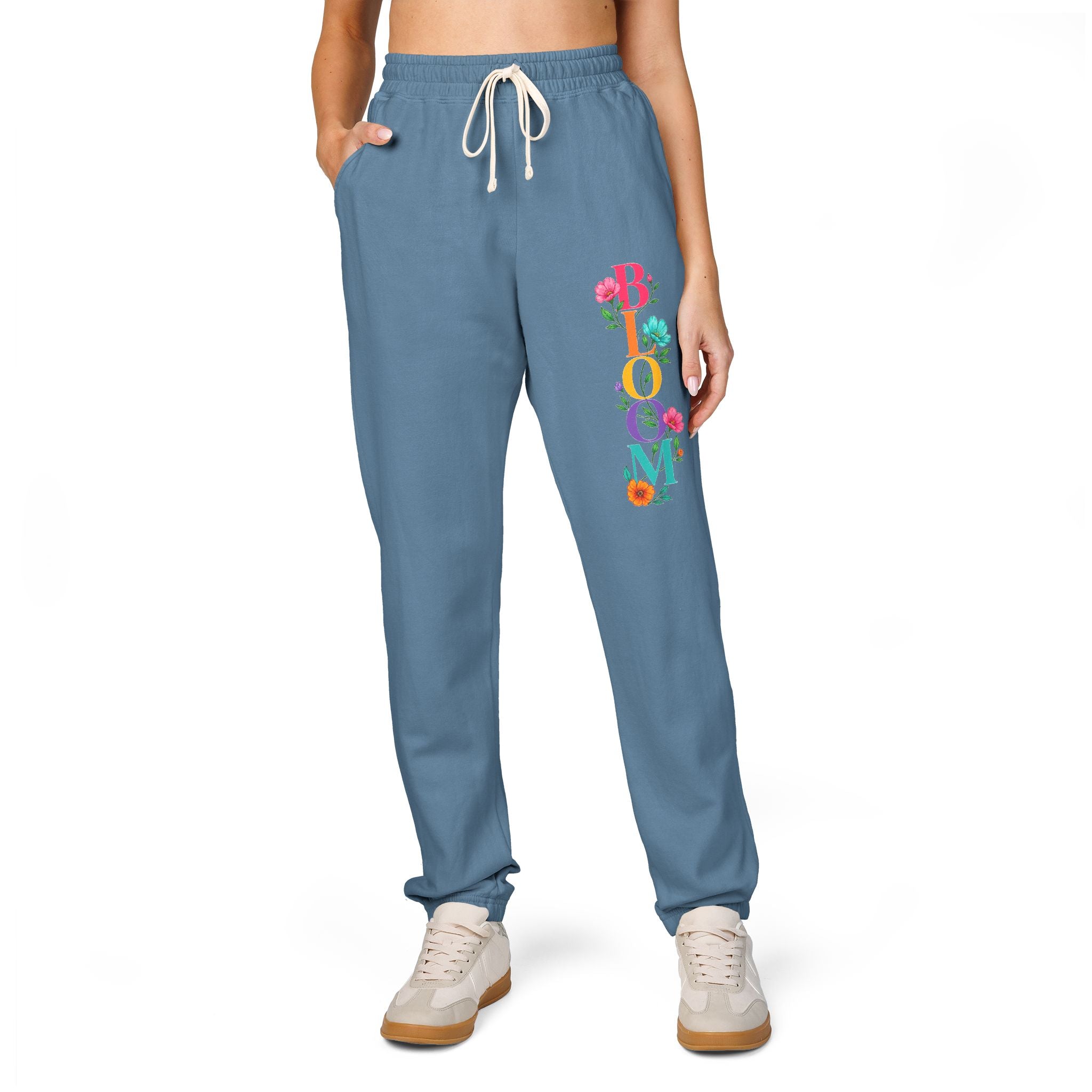Blue sweatpants with colorful 'Bloom' text worn by a person on a white background