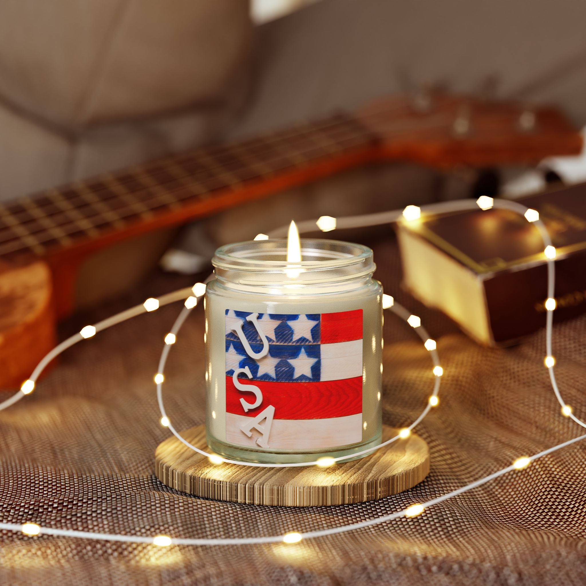 Candle with a USA label on a wooden coaster surrounded by string lights, with a guitar in the background.