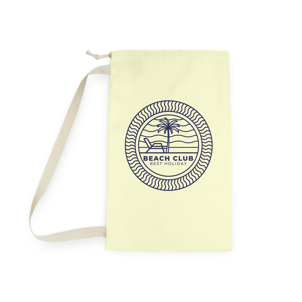 A pale yellow canvas tote bag with a beige shoulder strap, featuring a navy blue circular graphic on the front with a palm tree, beach chair, and the text 'BEACH CLUB BEST HOLIDAY'.