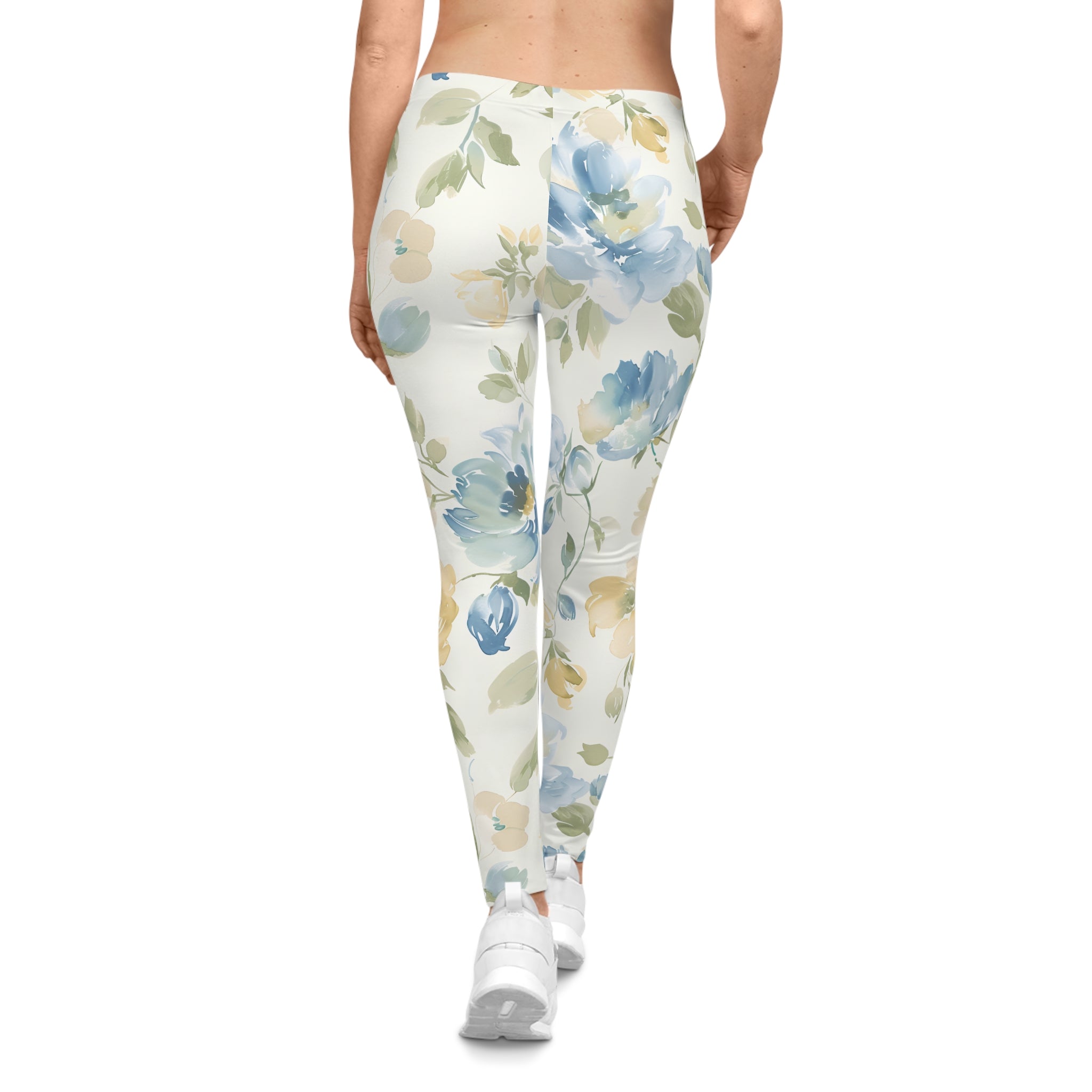 A person shown from the back wearing high-waisted leggings with a watercolor floral print in blue, green, and beige on an off-white background, paired with white sneakers against a plain white studio background.