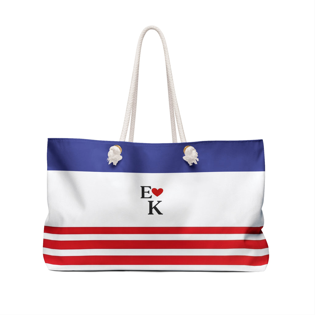 A tote bag with a patriotic red, white, and blue horizontal stripe design, featuring a blue top band, white middle section, red and white bottom stripes, white rope handles, and a central 'E [heart] K' graphic.