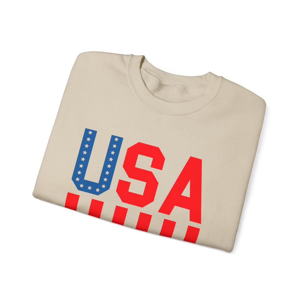 A beige crewneck sweatshirt folded neatly, featuring a bold 'USA' graphic on the front. The letter 'U' is filled with white stars on a blue background, while 'S' and 'A' are solid red, and the bottom has red and white stripes.