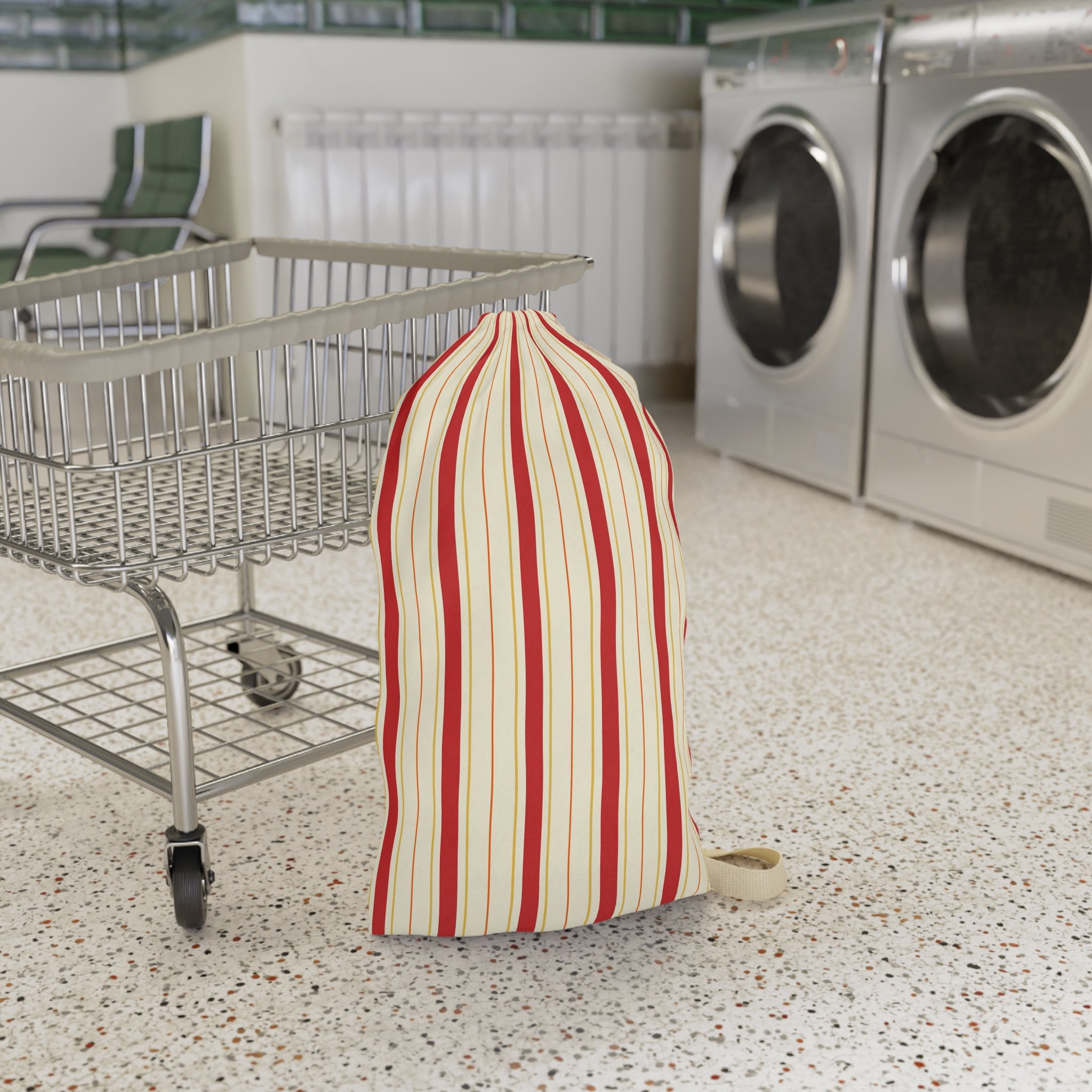 A striped laundry bag with red and cream vertical stripes sits on a speckled floor next to a metal shopping cart, with washing machines in the background.