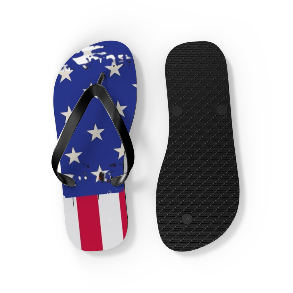A pair of flip-flops shown on a white background, with one sandal upright to display the top featuring a distressed American flag design in blue, white, and red, and the other showing the black textured sole.