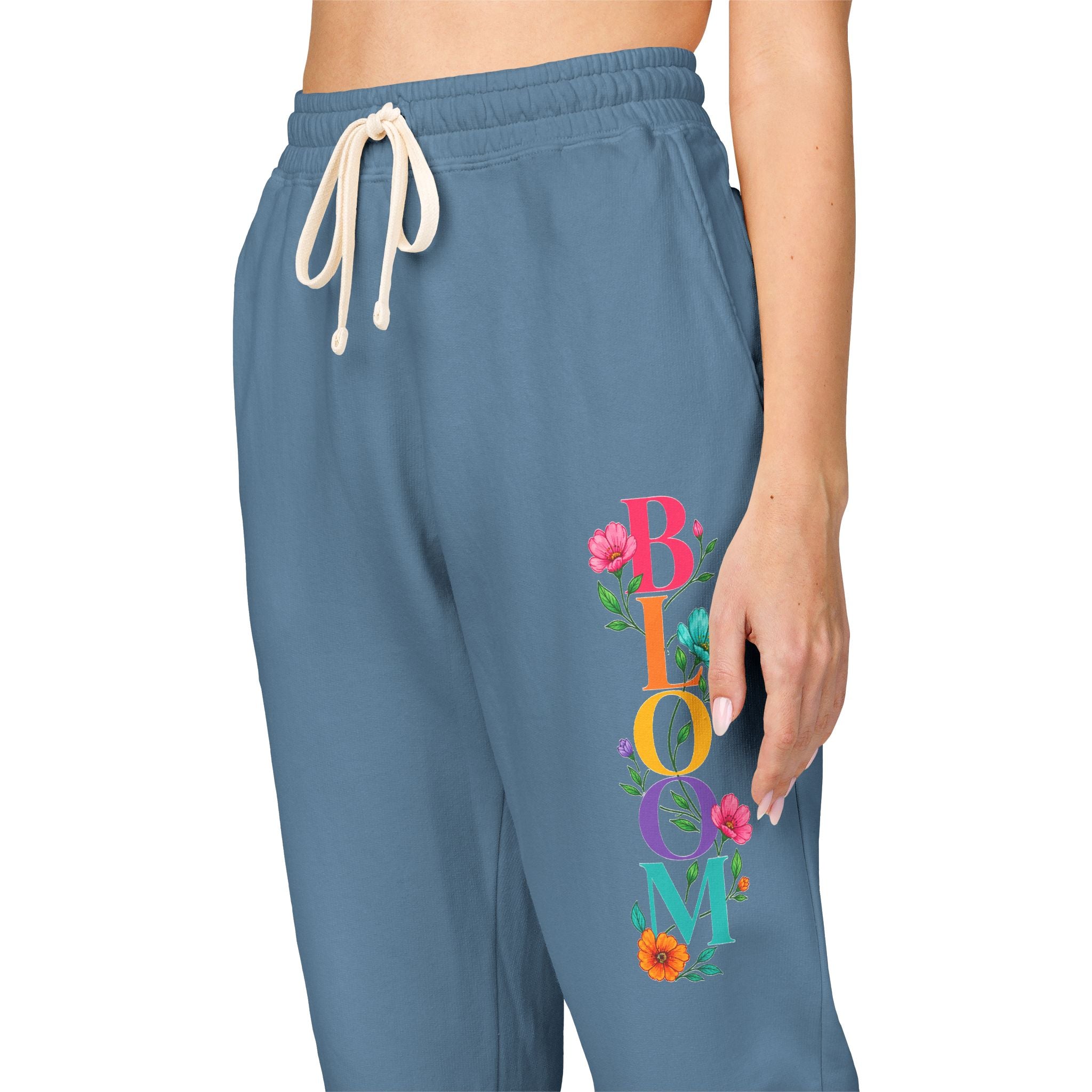 Blue sweatpants with 'BLOOM' text and floral designs on a white background