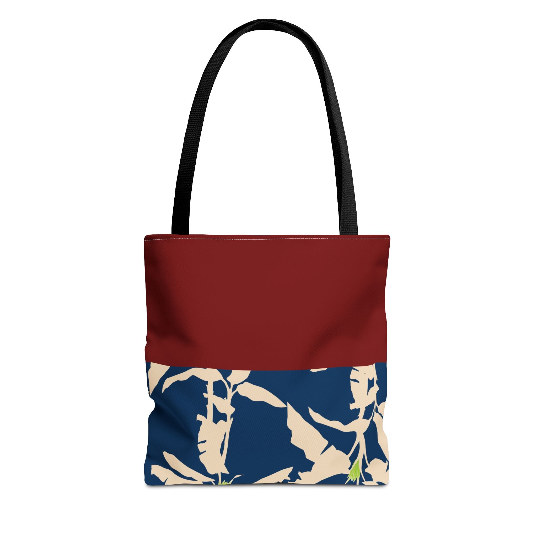 A tote bag with a solid dark red upper section, black shoulder straps, and a navy blue lower section featuring a beige tropical leaf pattern.