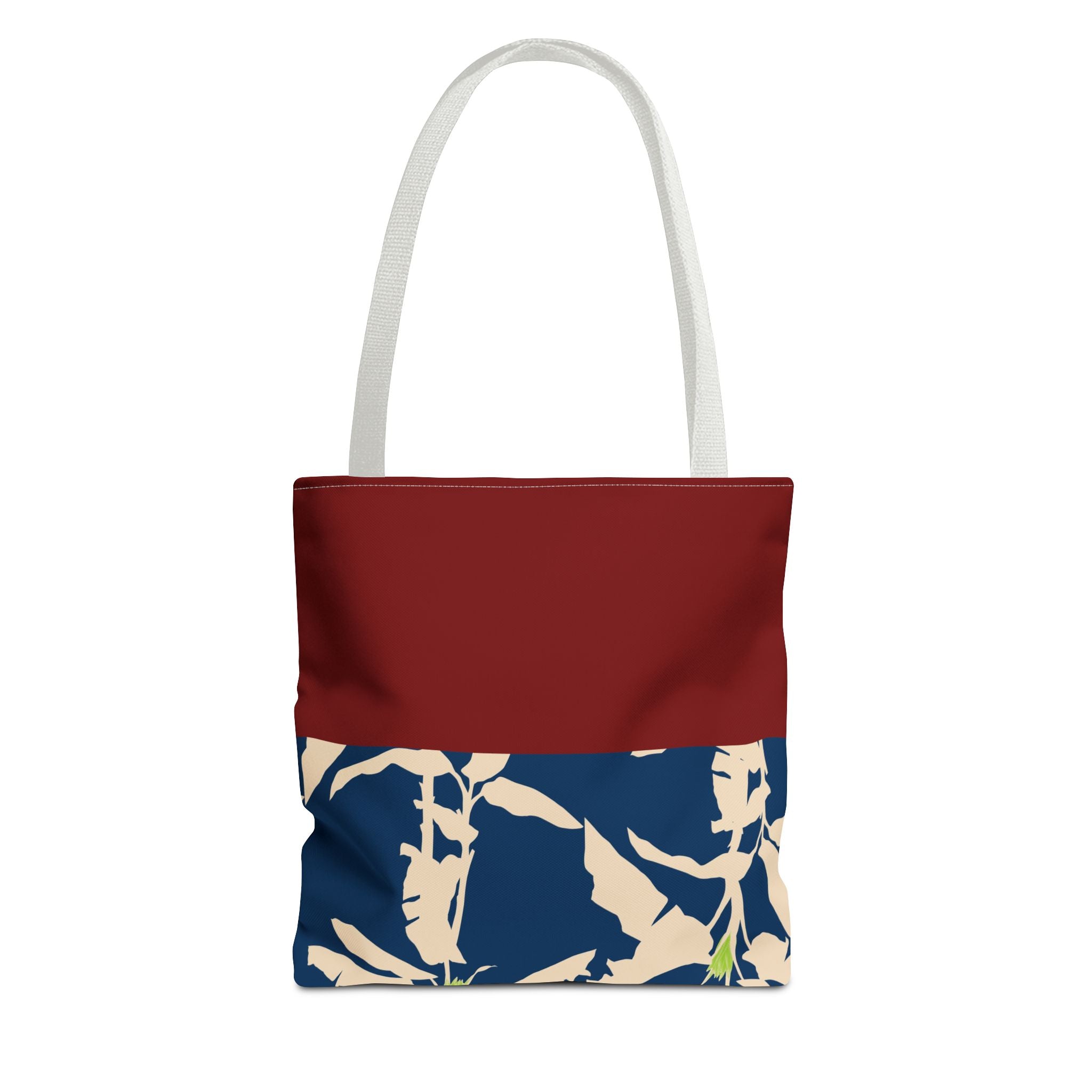 A tote bag with a solid dark red top half and a navy blue bottom half featuring a beige tropical leaf pattern, with white shoulder straps, shown on a plain white background.