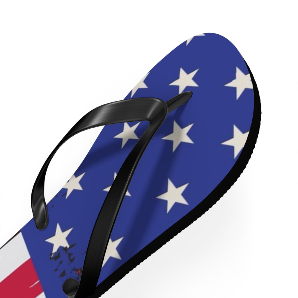 A single flip-flop sandal shown on a plain white background, featuring a blue footbed printed with white stars and a small portion of a red-and-white striped section, plus black straps.