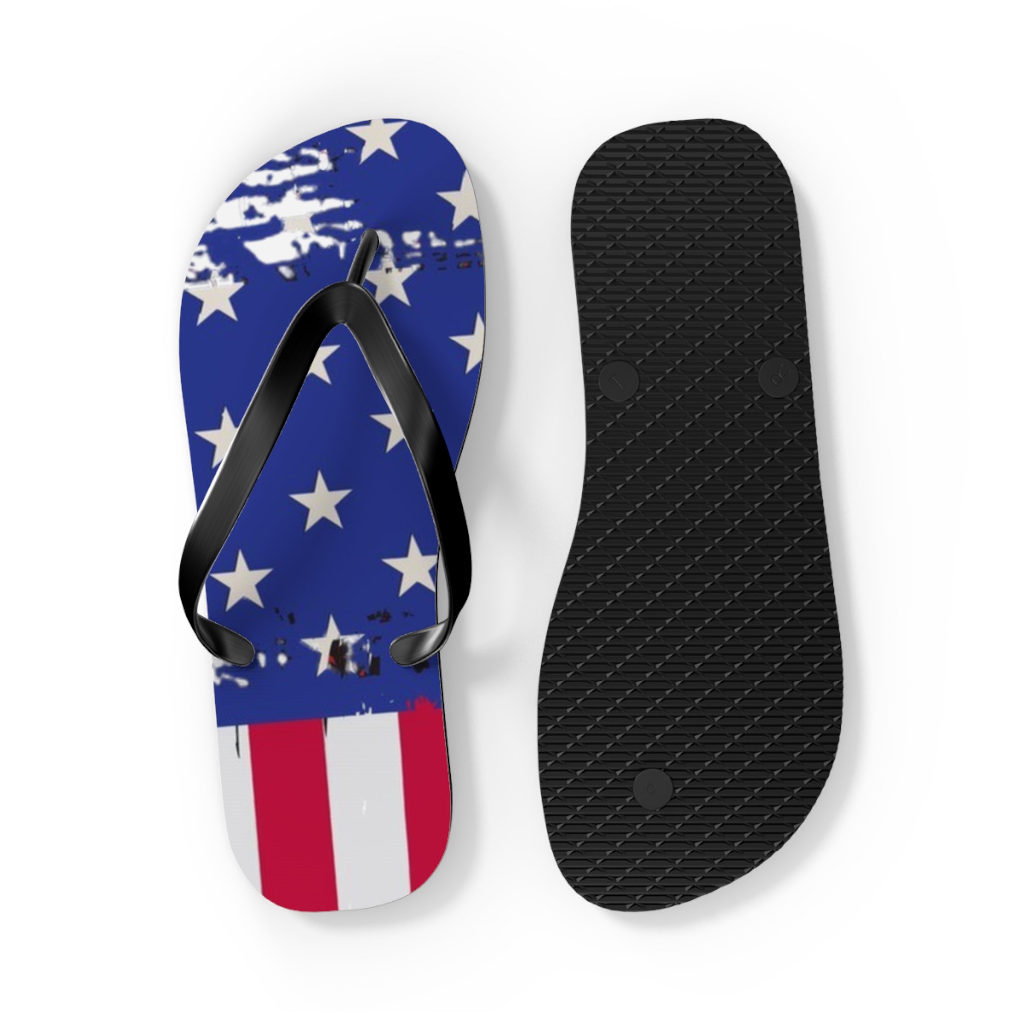 A pair of flip-flops shown on a white background, with one sandal displaying a distressed American flag design in blue, white, and red, and the other showing the black textured sole.