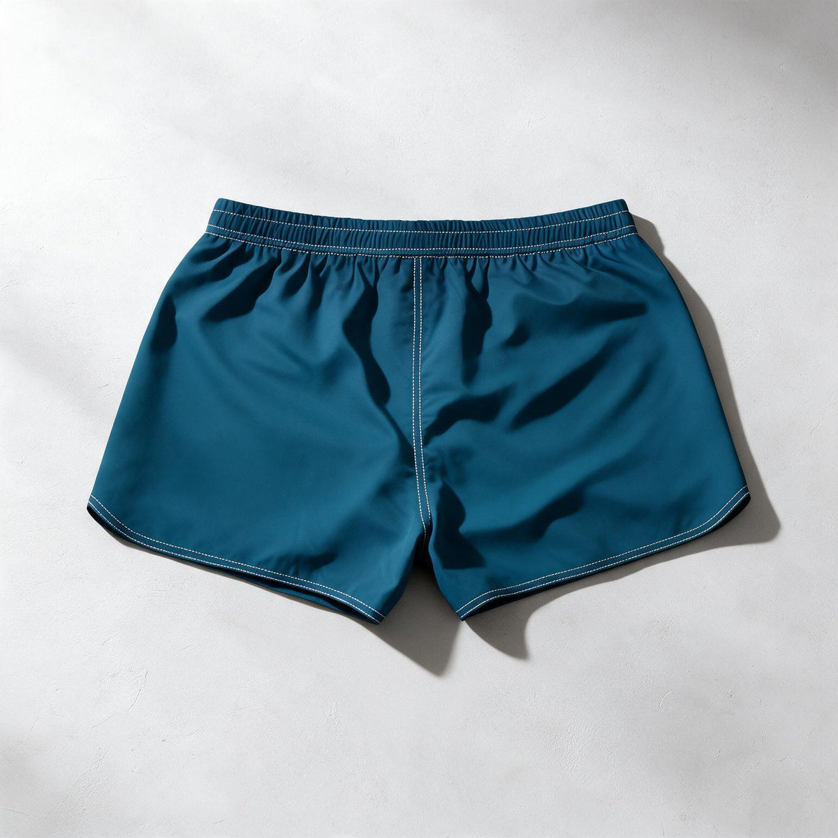 A pair of teal blue athletic shorts with an elastic waistband, laid flat on a light gray textured surface with soft shadows.