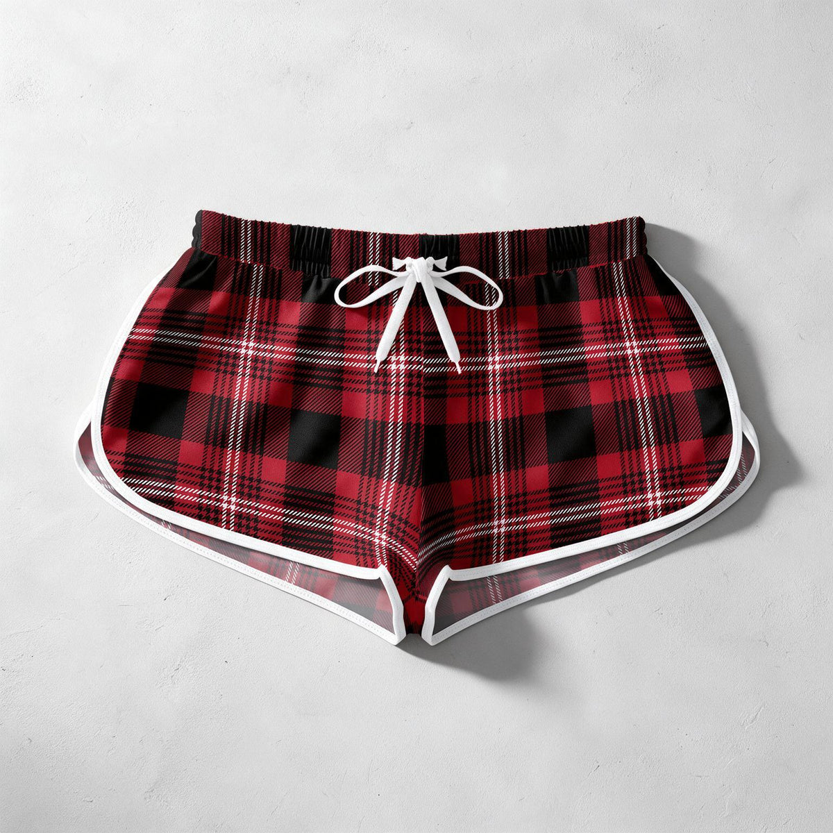 Red and black plaid shorts with a white drawstring and white piping trim, laid flat on a light gray textured background.