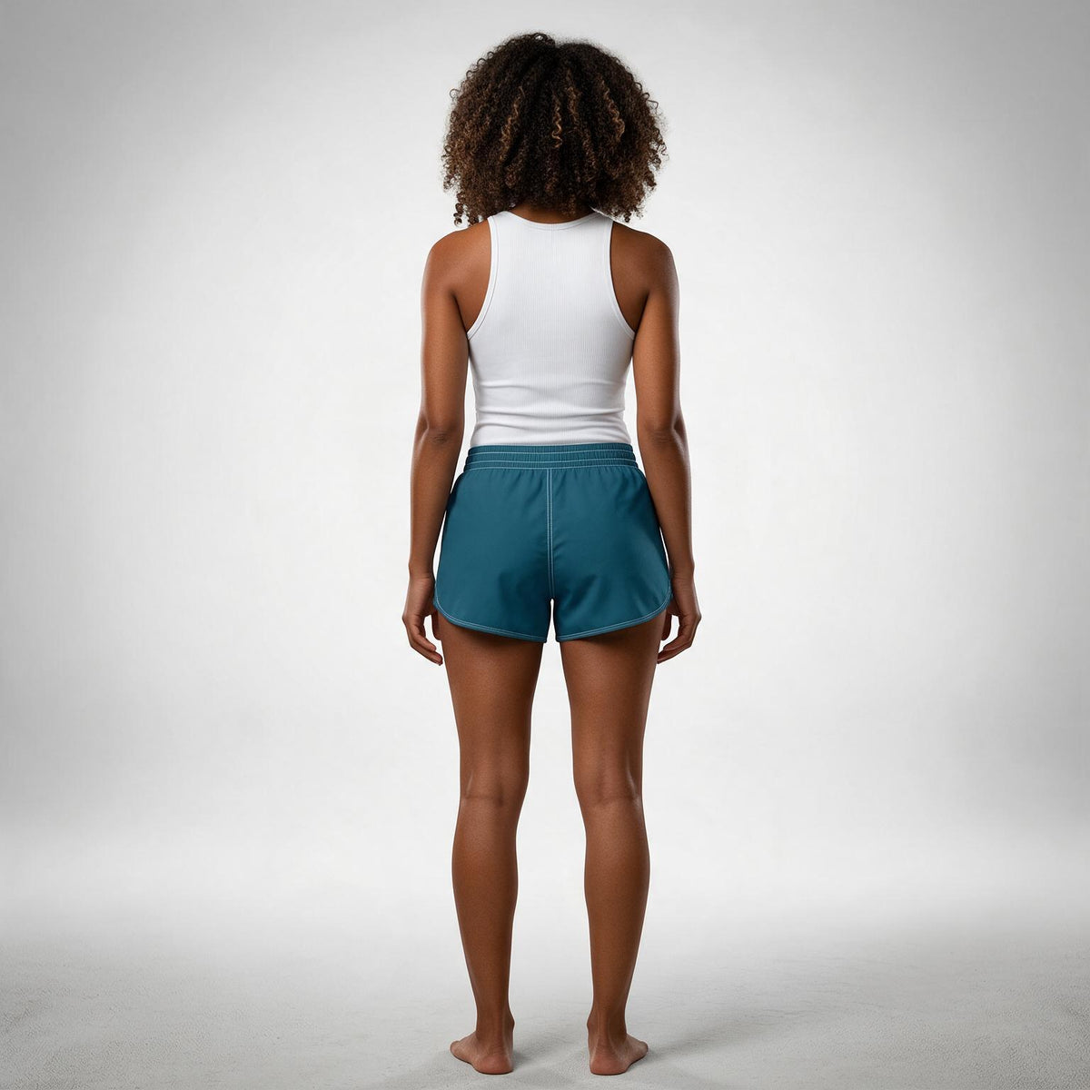 A woman is shown from behind wearing a white tank top and teal athletic shorts against a light gray studio background.