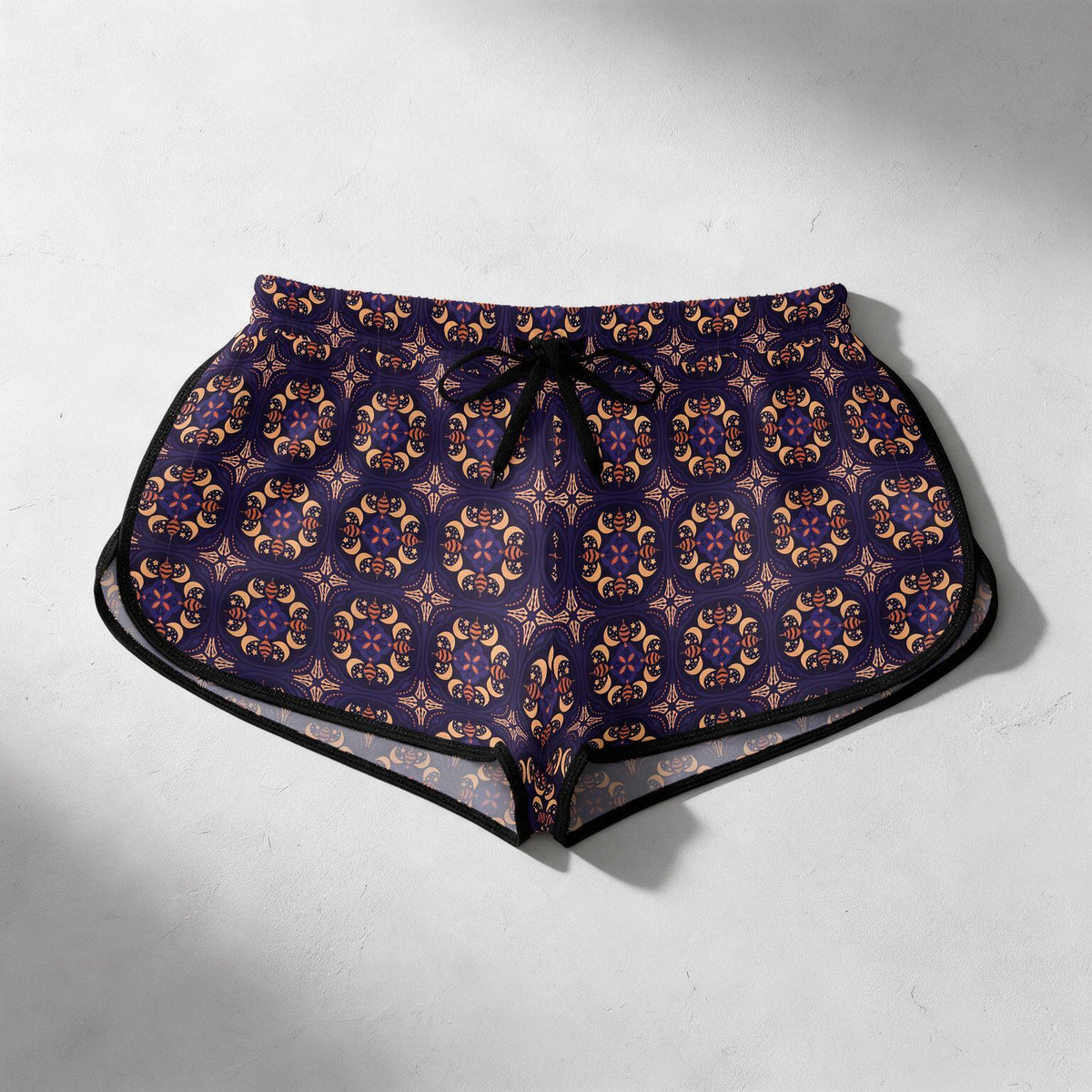 A pair of women's swim trunks featuring a dark purple and gold geometric pattern, with a black drawstring waist and black trim, laid flat on a light gray textured background.