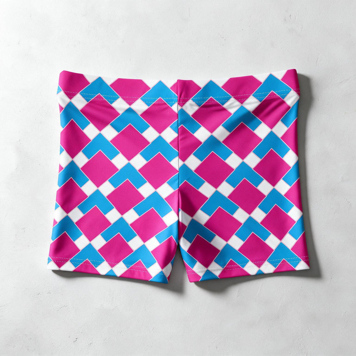A pair of athletic shorts featuring a bold geometric pattern of pink, blue, and white diamonds, laid flat on a light gray textured surface.