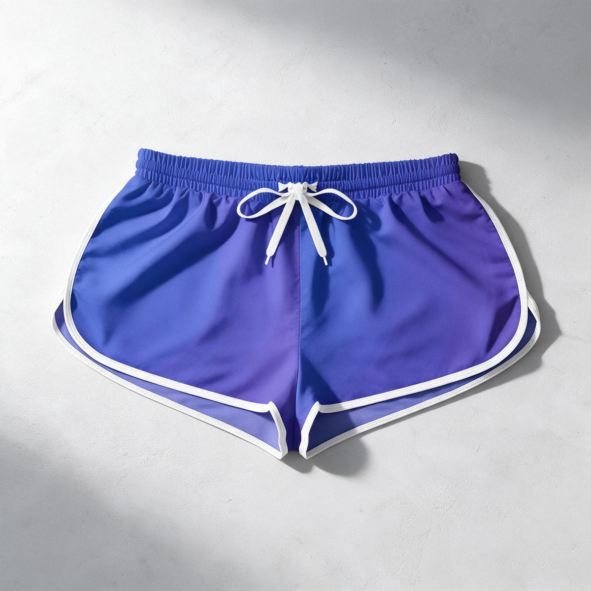A pair of athletic shorts with a purple-to-blue gradient body, white piping along the edges, and a white drawstring waist, laid flat on a light gray textured surface.