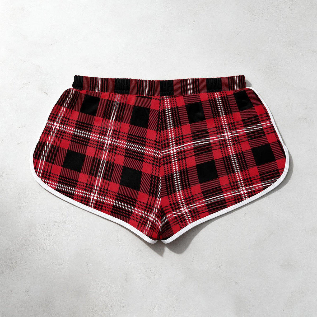 Red and black plaid shorts with a white border trim, laid flat on a light gray textured background.