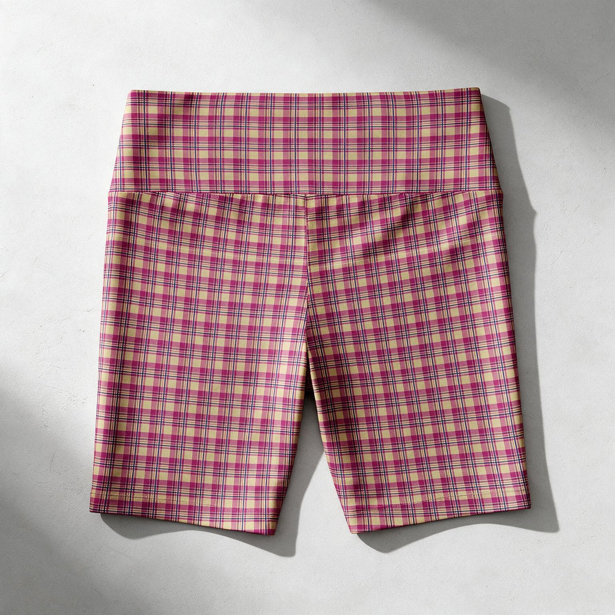 A pair of women's biker shorts with a pink, red, and beige plaid pattern, laid flat on a light gray background with soft shadows.