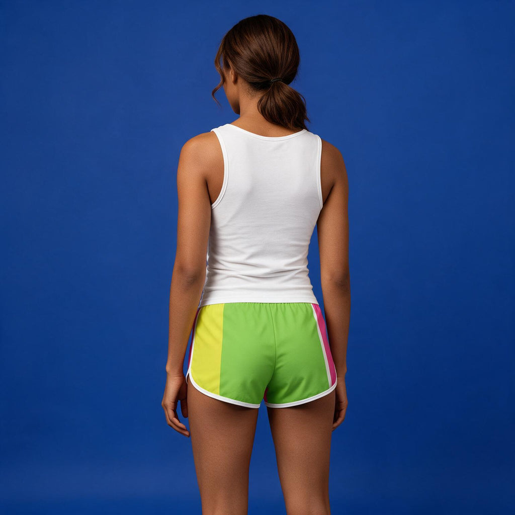 A woman shown from behind wearing bright color-blocked athletic shorts with green, yellow, and pink panels, paired with a white tank top, against a solid blue studio background.
