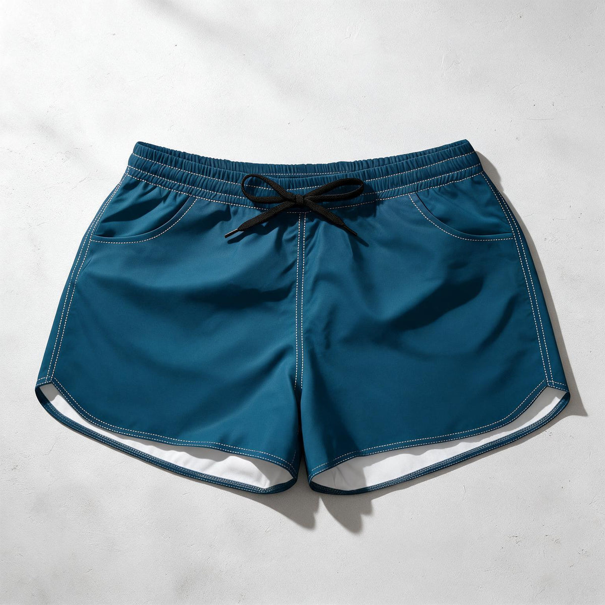 A pair of teal blue athletic shorts with a black drawstring waist, laid flat on a light gray textured background.