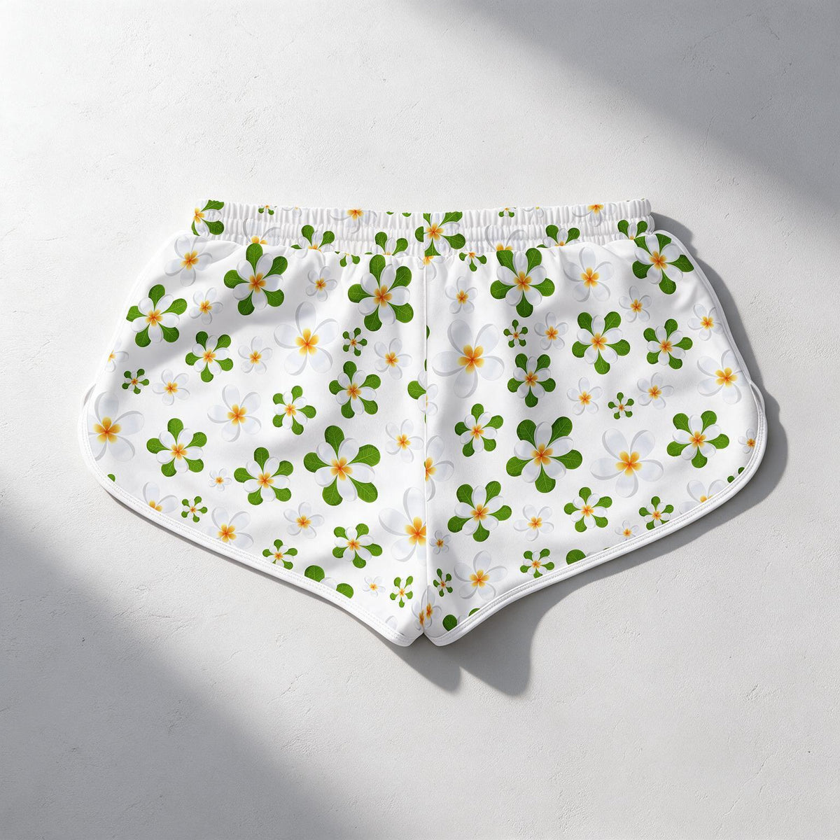 White athletic shorts with a green and yellow floral pattern, laid flat on a light gray surface with soft shadows.