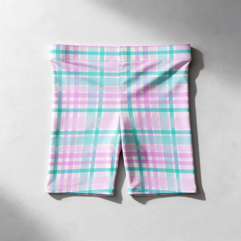 Pink and turquoise plaid athletic shorts laid flat on a light gray concrete surface.