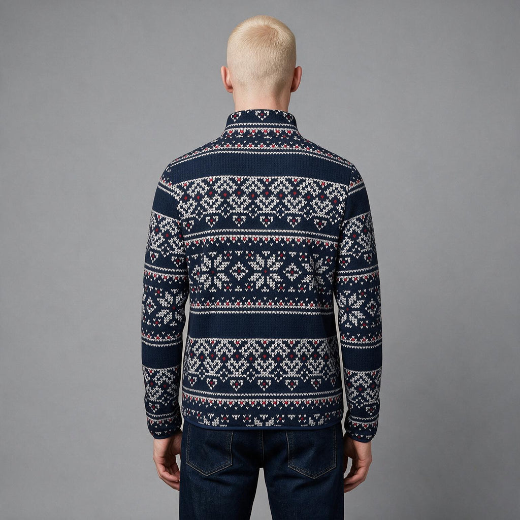 A man viewed from behind wearing a navy blue knit sweater with a white and red Nordic/Fair Isle pattern, paired with dark blue jeans, against a solid gray studio background.