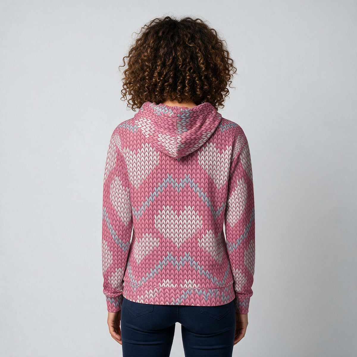 A person viewed from the back wearing a pink, white, and light blue patterned knit hoodie with dark blue jeans, set against a plain light gray background.