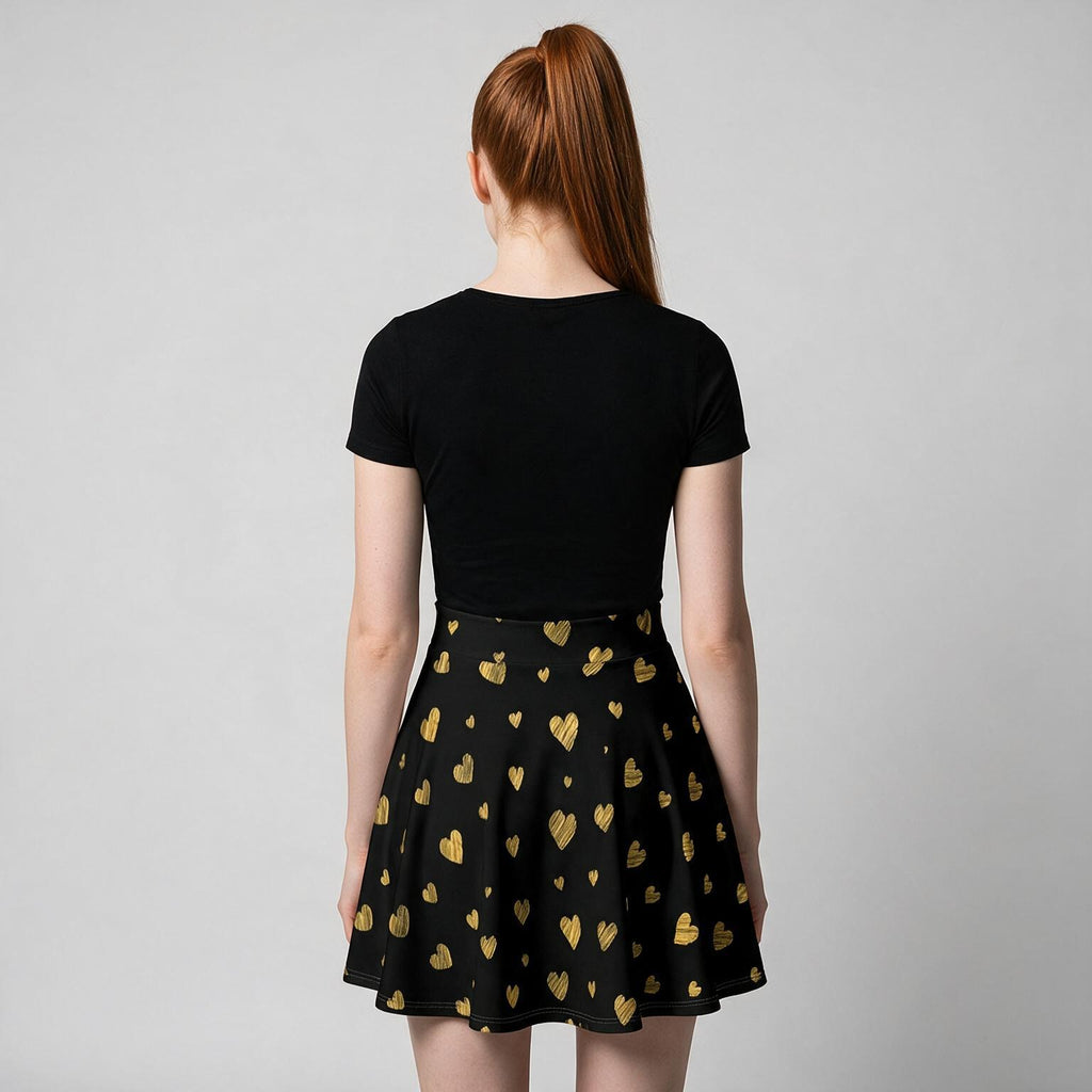 A woman viewed from behind wearing a black short-sleeve top and a black flared skirt with a repeating metallic gold heart pattern, against a light gray studio background.