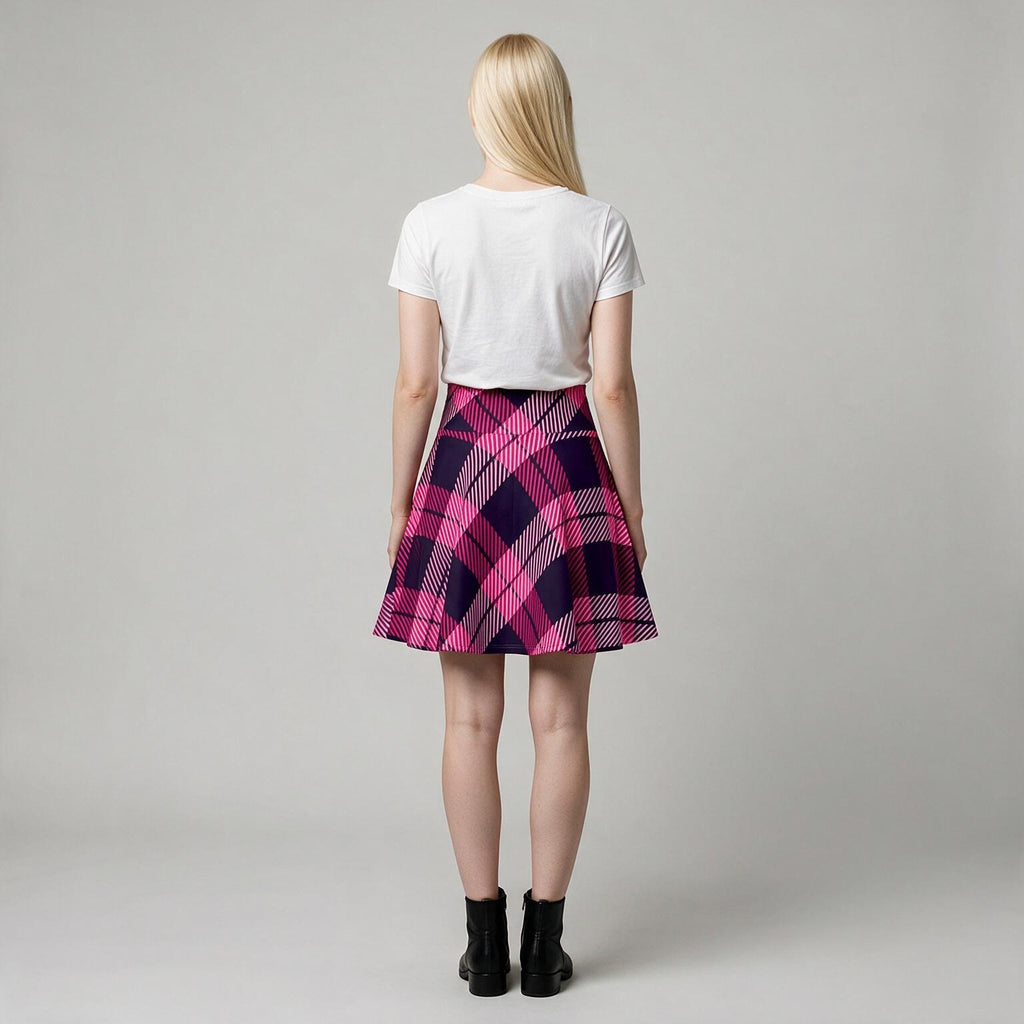 A woman viewed from behind wearing a white short-sleeve crop top and a pink and purple plaid pleated mini skirt, paired with black ankle boots, against a light gray studio background.
