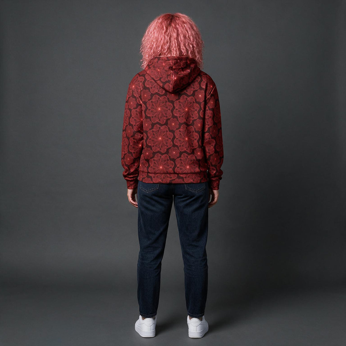 A person standing with their back to the camera, wearing a dark red hoodie with a black rose pattern, dark blue jeans, and white sneakers, set against a dark gray studio background.