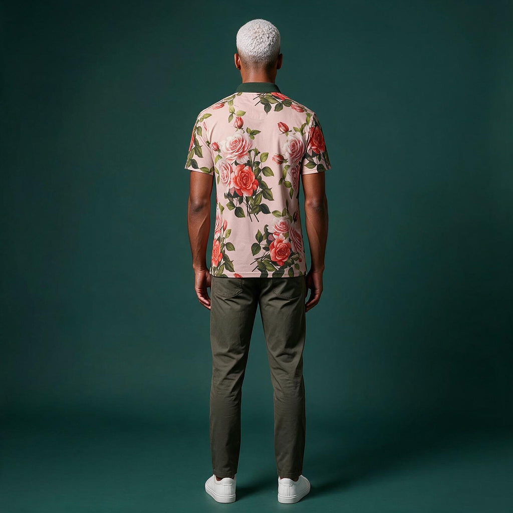 A man viewed from behind wearing a short-sleeve floral t-shirt with pink roses and green leaves, paired with olive green pants and white sneakers, set against a dark teal studio background.