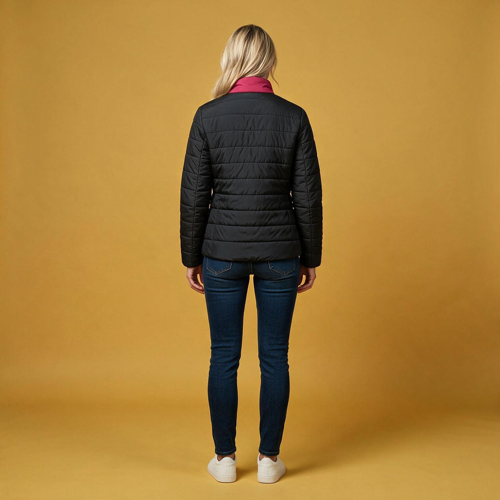 A woman is shown from behind wearing a black quilted puffer jacket, dark blue skinny jeans, and white sneakers, standing against a solid mustard yellow studio background.