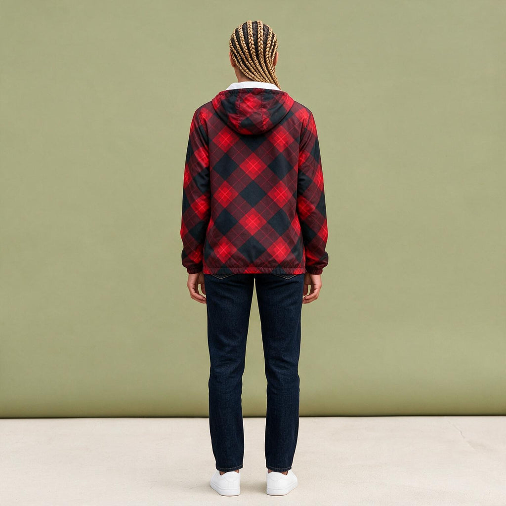 A person viewed from the back wearing a red and black buffalo plaid hooded jacket, dark blue jeans, and white sneakers, standing against a solid sage green wall.